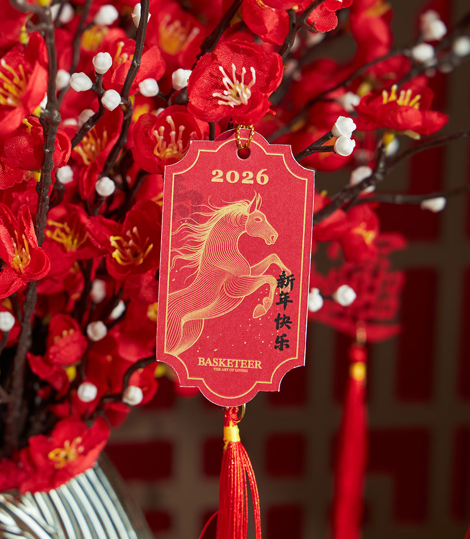 Basketeer premium hamper accent: Red cherry blossom branches in vase. Horse-themed tag with tassel. Perfect luxury gift for Chinese New Year in Bangkok.