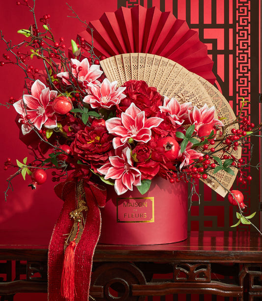 Basketeer's luxury gift for Chinese New Year: red floral arrangement with lilies and pomegranates, plus a bamboo fan in a festive red gift box. Perfect corporate gift Bangkok.