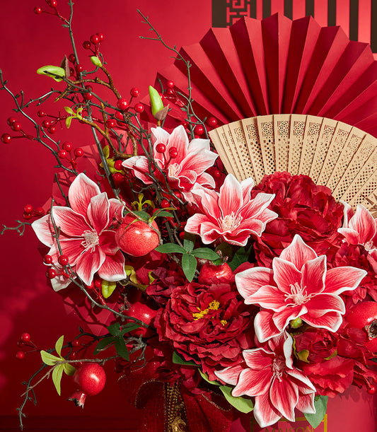 Red and gold Chinese New Year floral arrangement with peonies, magnolias, bamboo fans, and decorative pomegranates