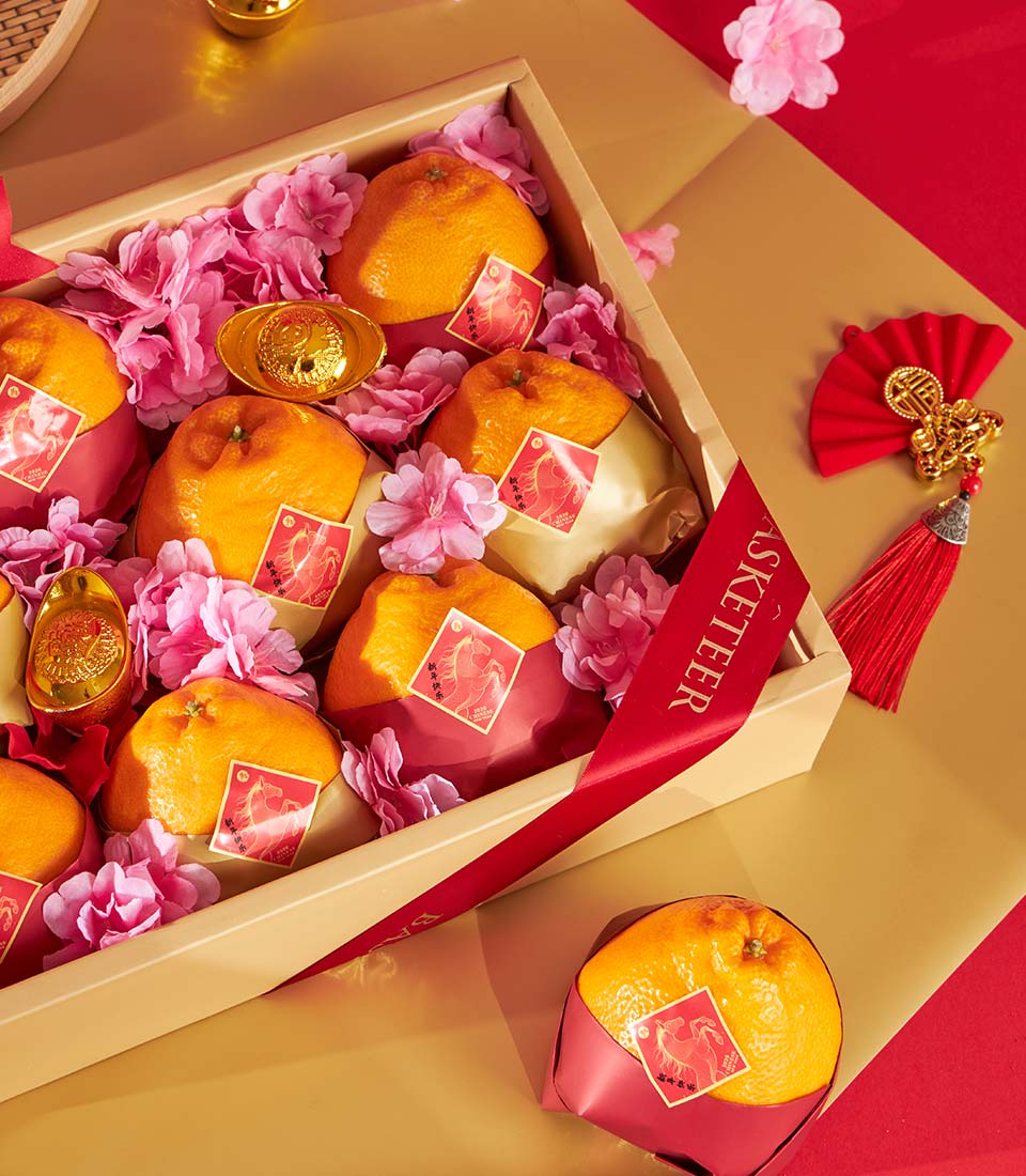 Golden Dekopon oranges with pink florals, red paper wrapping, and gold prosperity charms in luxury gift box