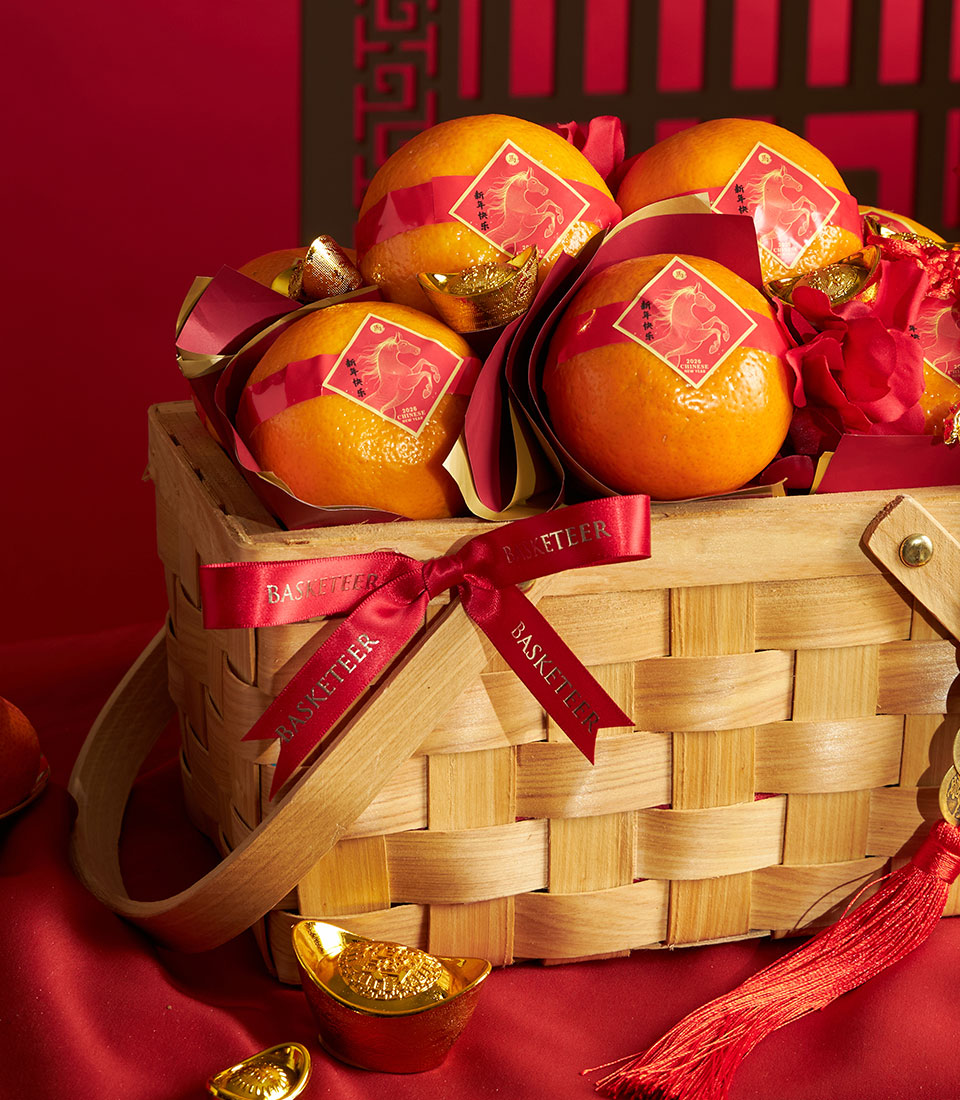 Woven wooden basket of individually wrapped Mandarin oranges with red ribbon, gold ingots, and festive Chinese New Year