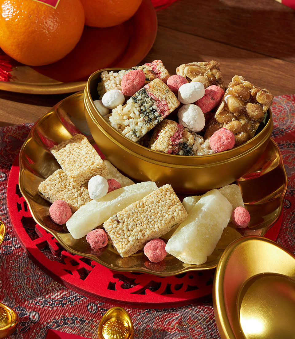 Festive golden bowl with mandarin oranges, peanut brittle, and sugar-dusted sweets for Chinese New Year celebration