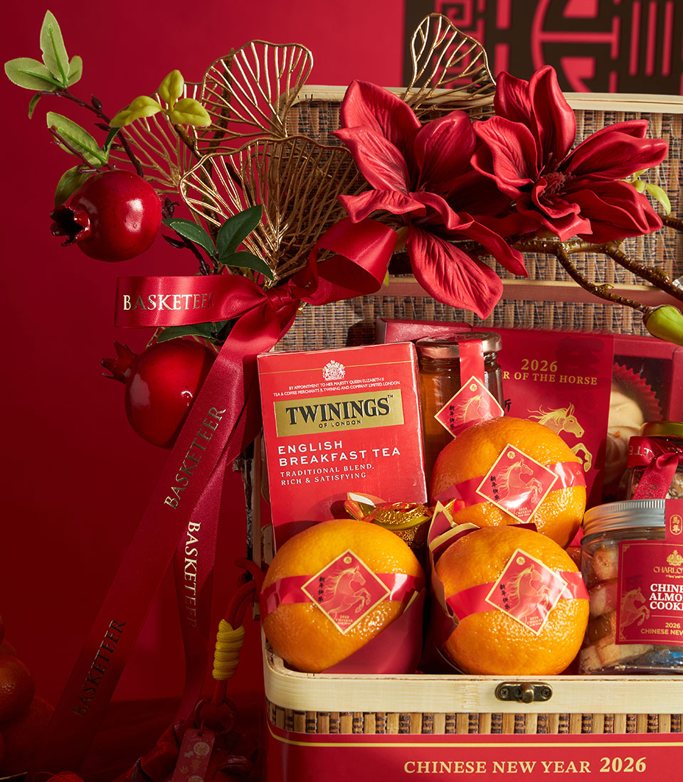 Woven gift basket with Twinings tea, mandarin oranges with red ribbons, almond cookies, red flower arrangement and gold