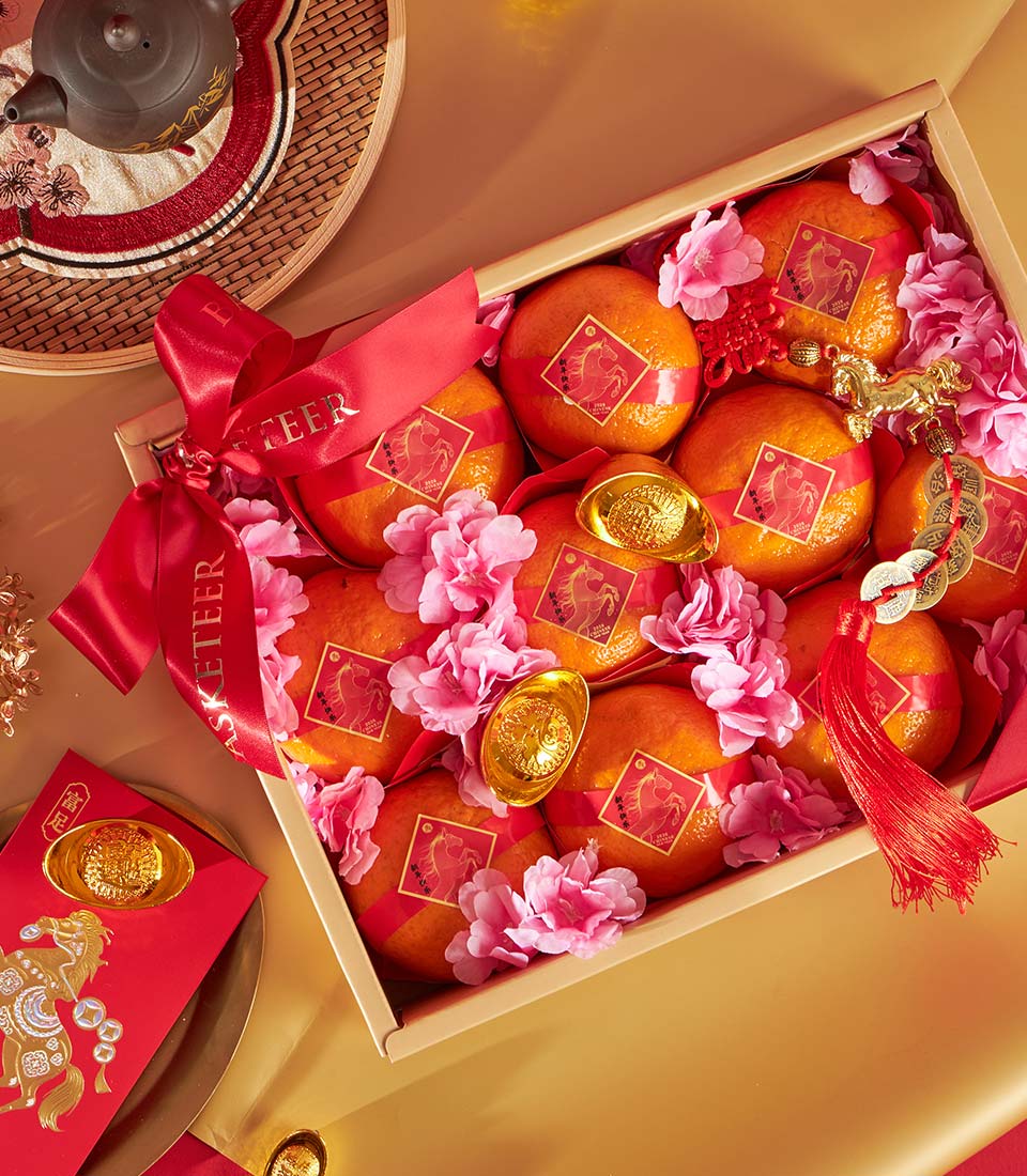 Premium mandarin orange gift box with red silk bands and gold horse charms, nestled with cherry blossoms and gold ingots for
