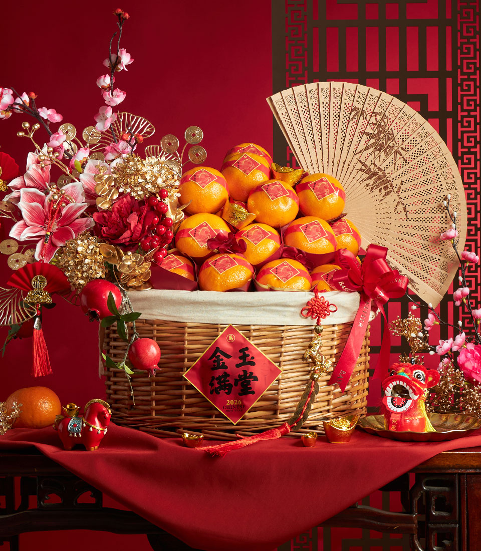 Luxury Chinese New Year gift basket overflowing with red-wrapped mandarin oranges, ornate bamboo fan, and festive gold