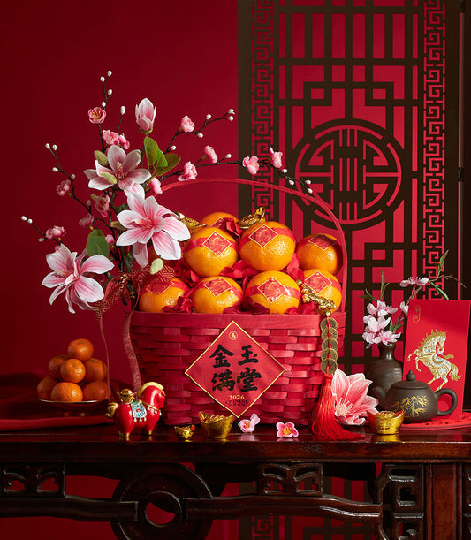 Vibrant red woven basket overflowing with fresh mandarin oranges and artificial pink magnolia flowers for Chinese New Year