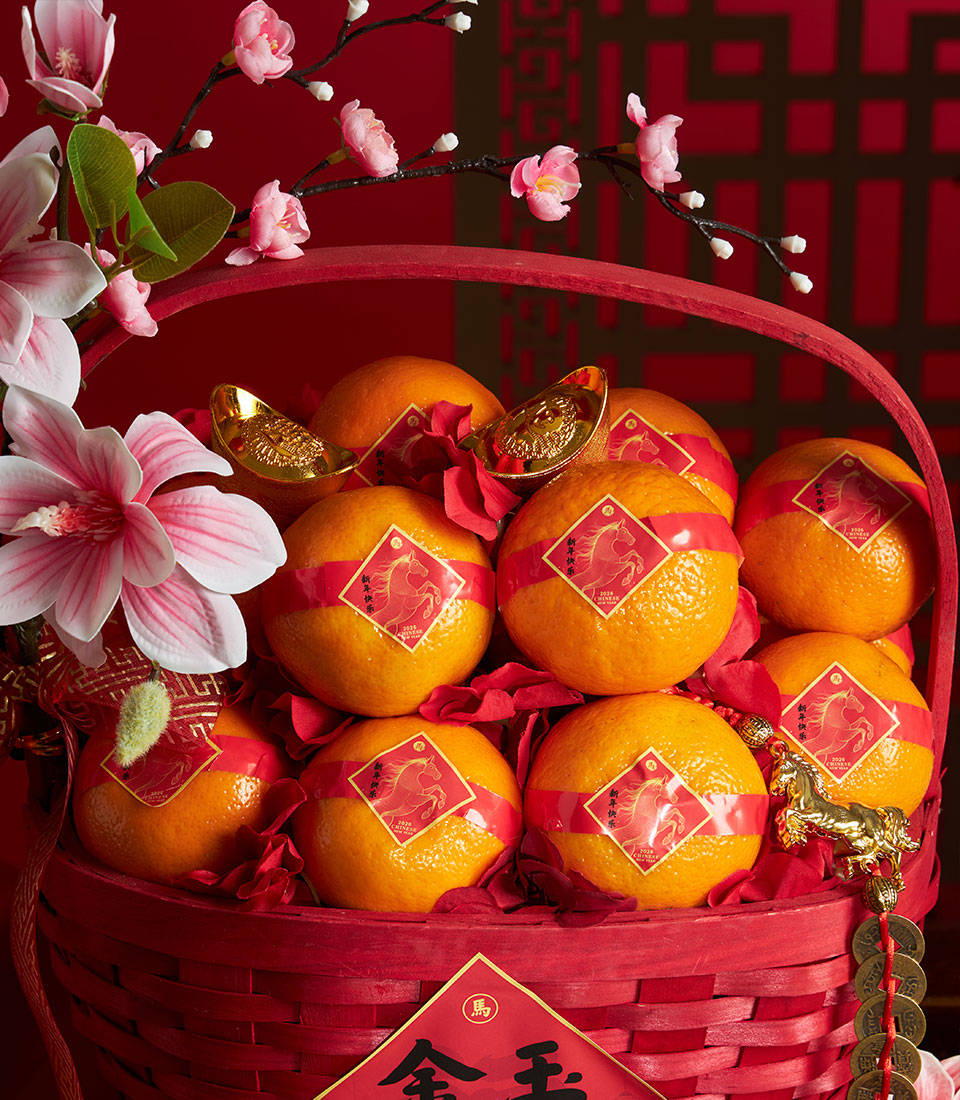 Red woven basket filled with mandarin oranges, gold ingots, and artificial flowers for Chinese New Year gifting