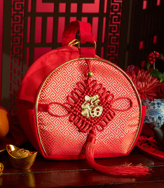 Red silk drawstring bag with gold geometric pattern and Fu character knot, paired with mandarin orange and traditional