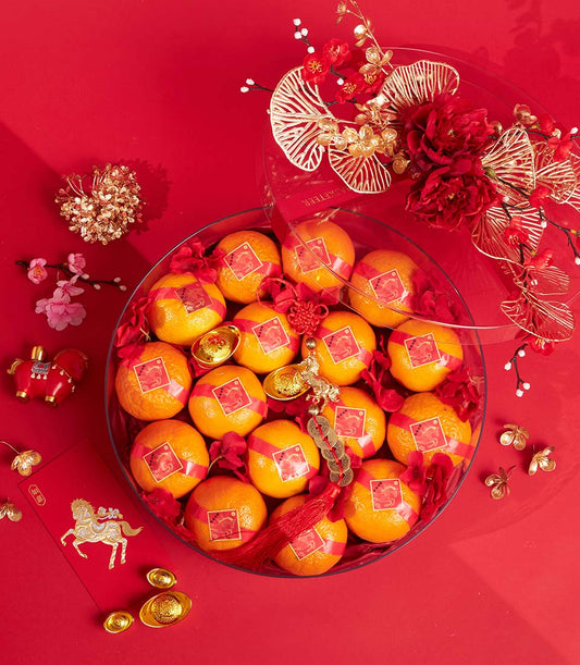 Premium mandarin oranges with red ribbon and gold auspicious labels in festive red and gold floral arrangement for Chinese