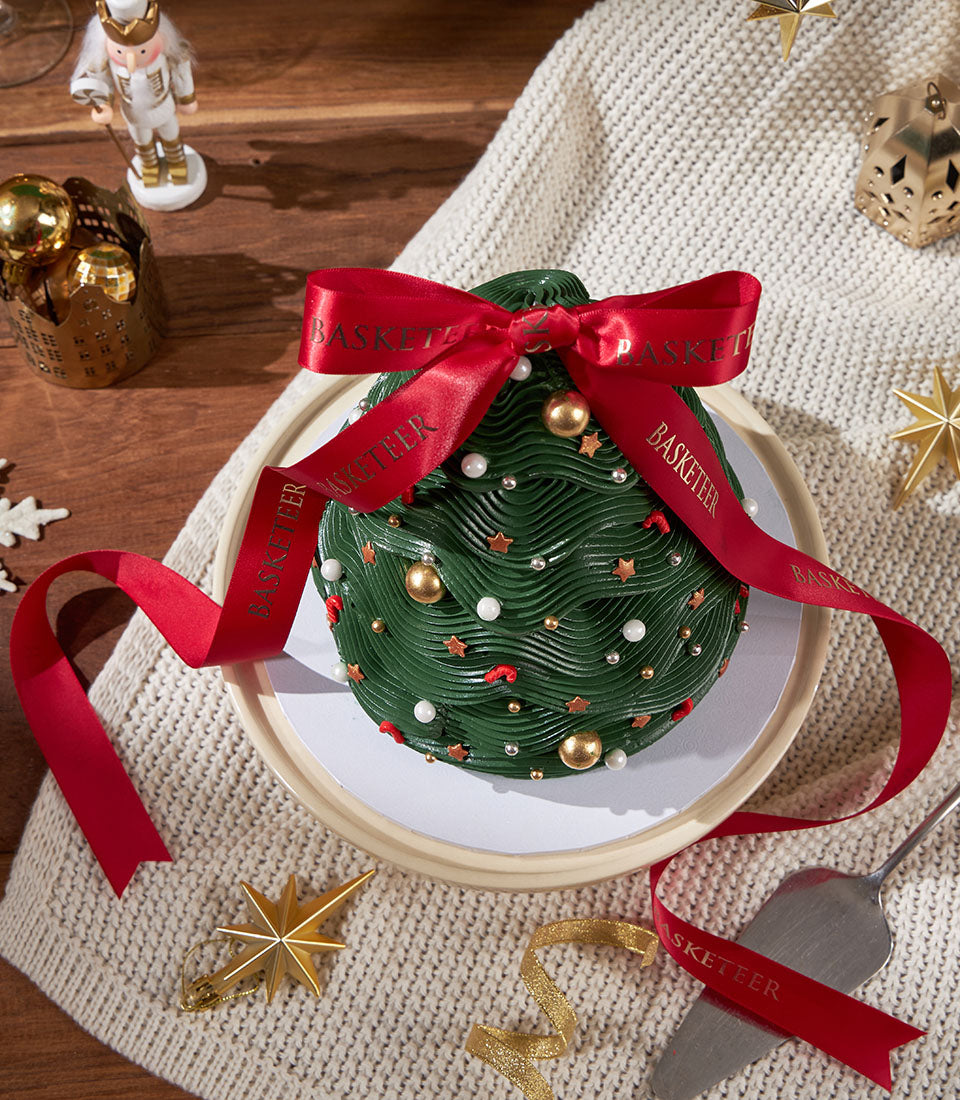 Festive green Christmas tree cake with gold pearl and star decorations, red candy accents, and red satin ribbon bow