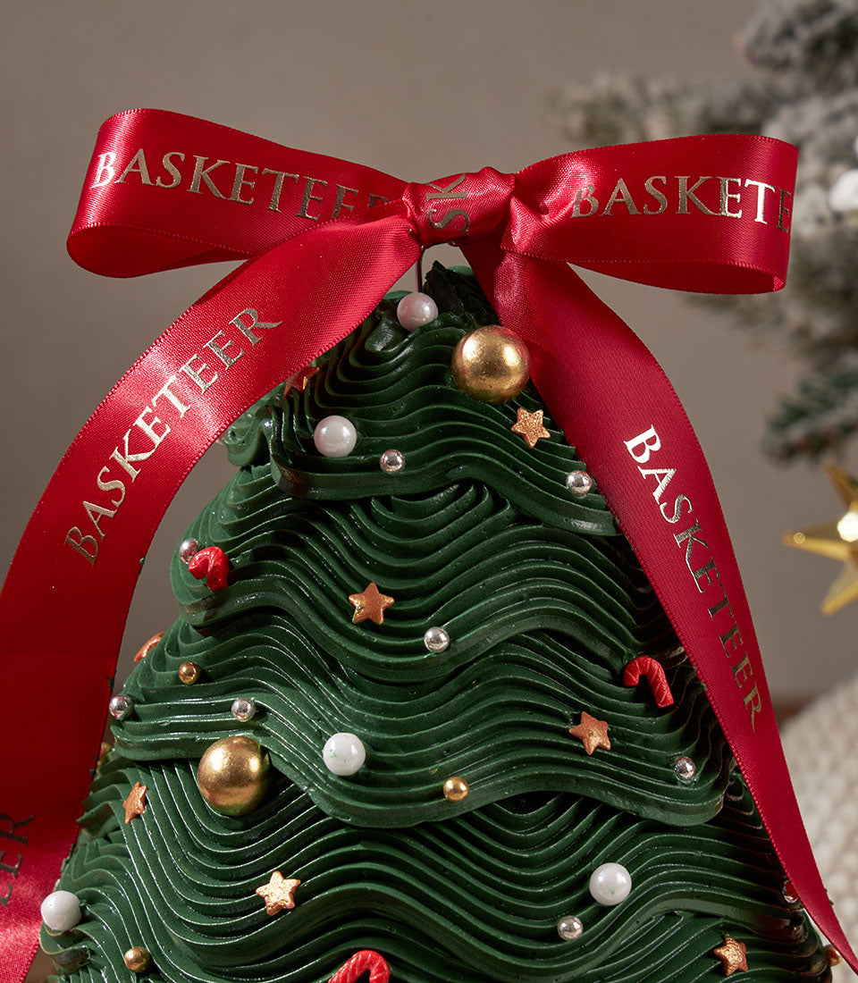 Artisan Christmas tree cake from Charlotte Bakery, Bangkok. Green buttercream frosting, candy cane accents, gold stars, and a bright red ribbon. Order a custom cake!