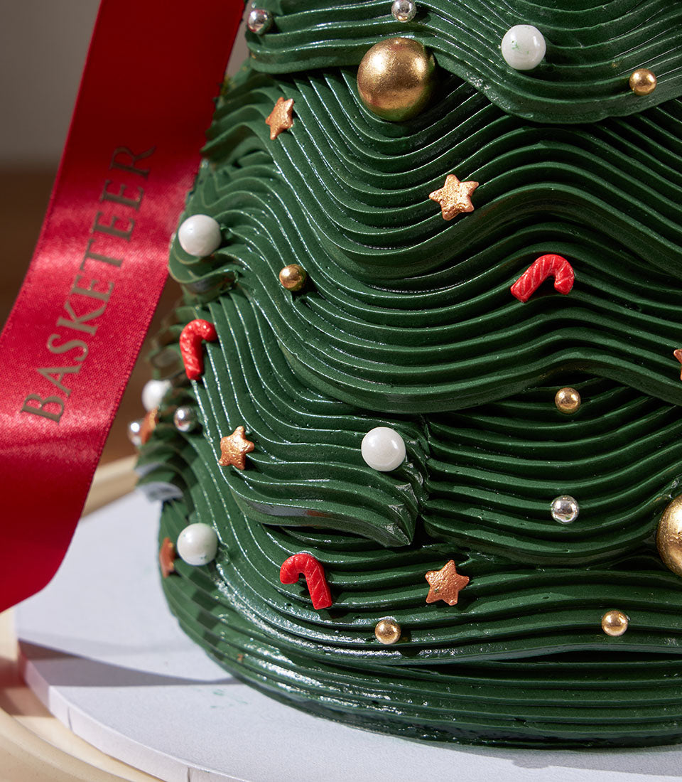 Chocolate Christmas tree cake with green frosting, gold and silver sprinkles, candy canes, and festive embellishments