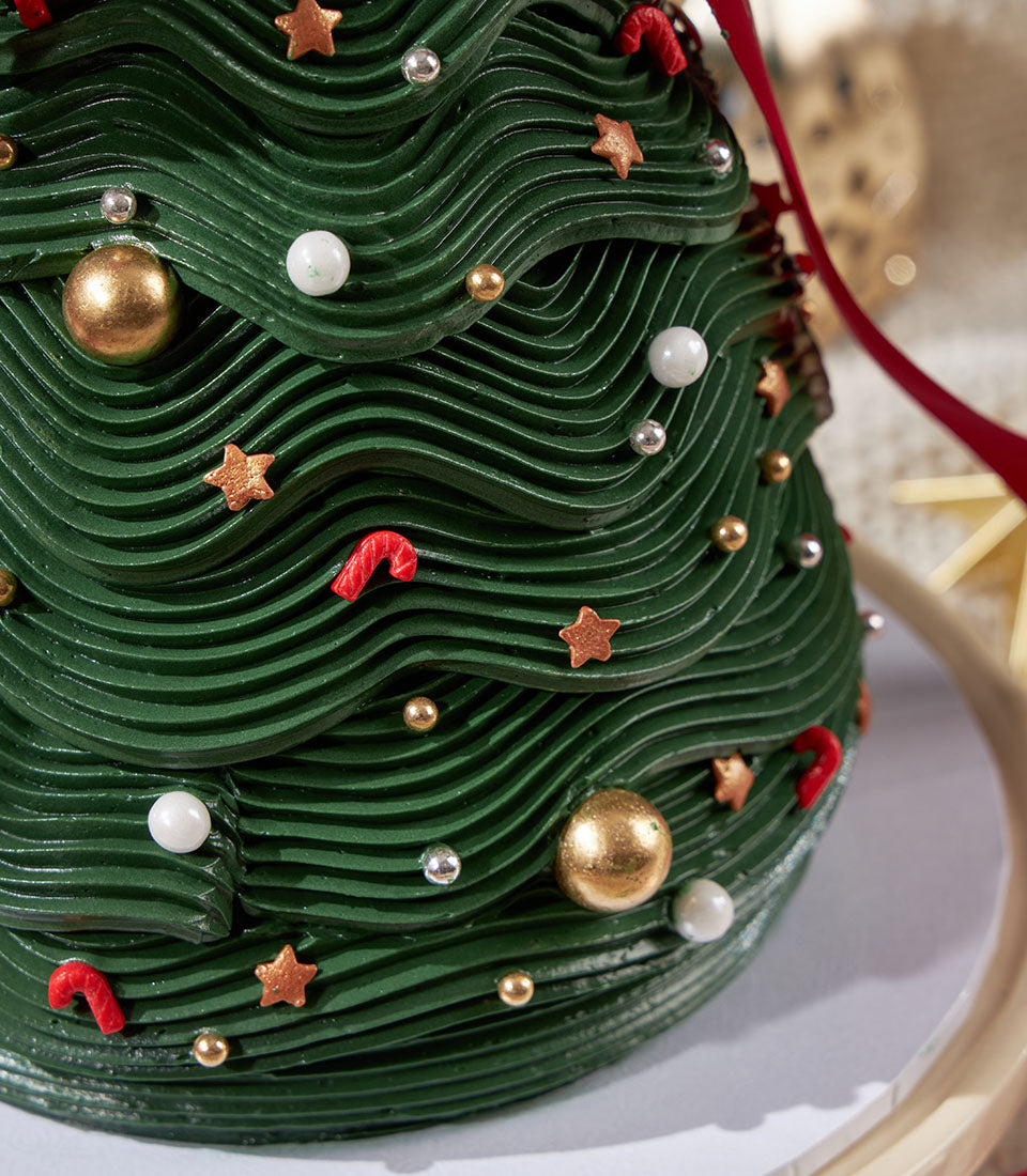 Charlotte Bakery Christmas tree cake, a delightful artisan creation. Green buttercream frosting, candy cane & star sprinkles, gold ornaments. Order custom cake Bangkok!
