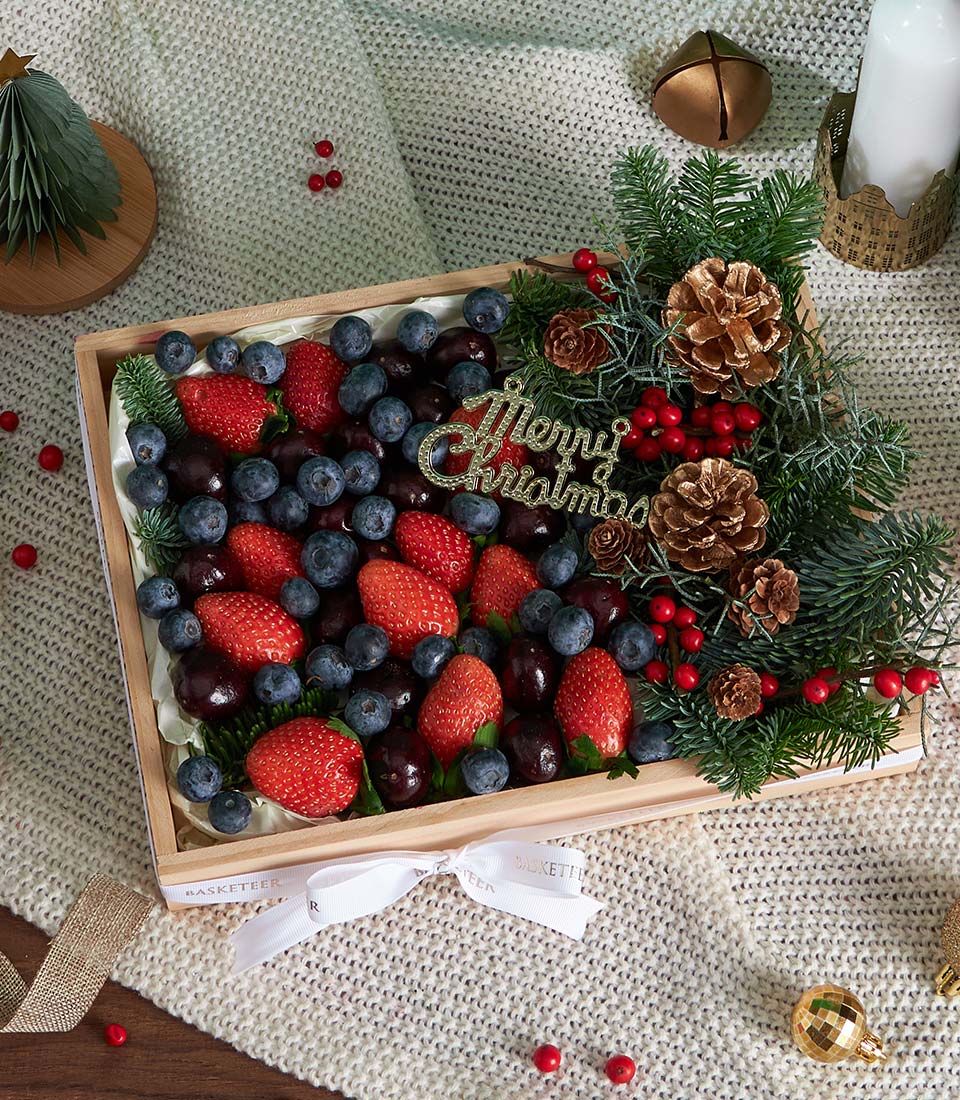 Festive berry fruit gift box with strawberries, blueberries, cherries, pine branches, and gold ornament for Christmas