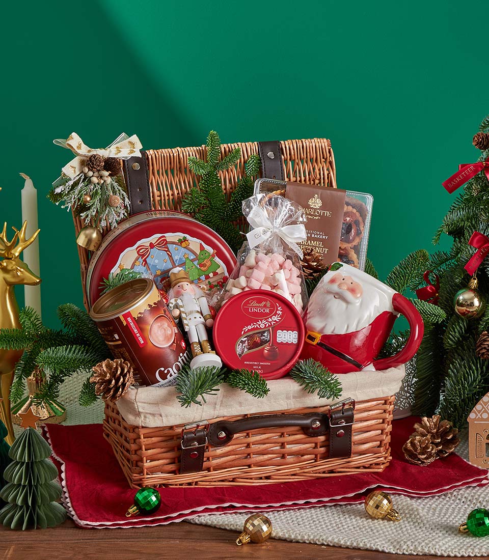 Woven wicker Christmas hamper filled with chocolate, hot chocolate, marshmallows, biscuits, and festive treats with pine