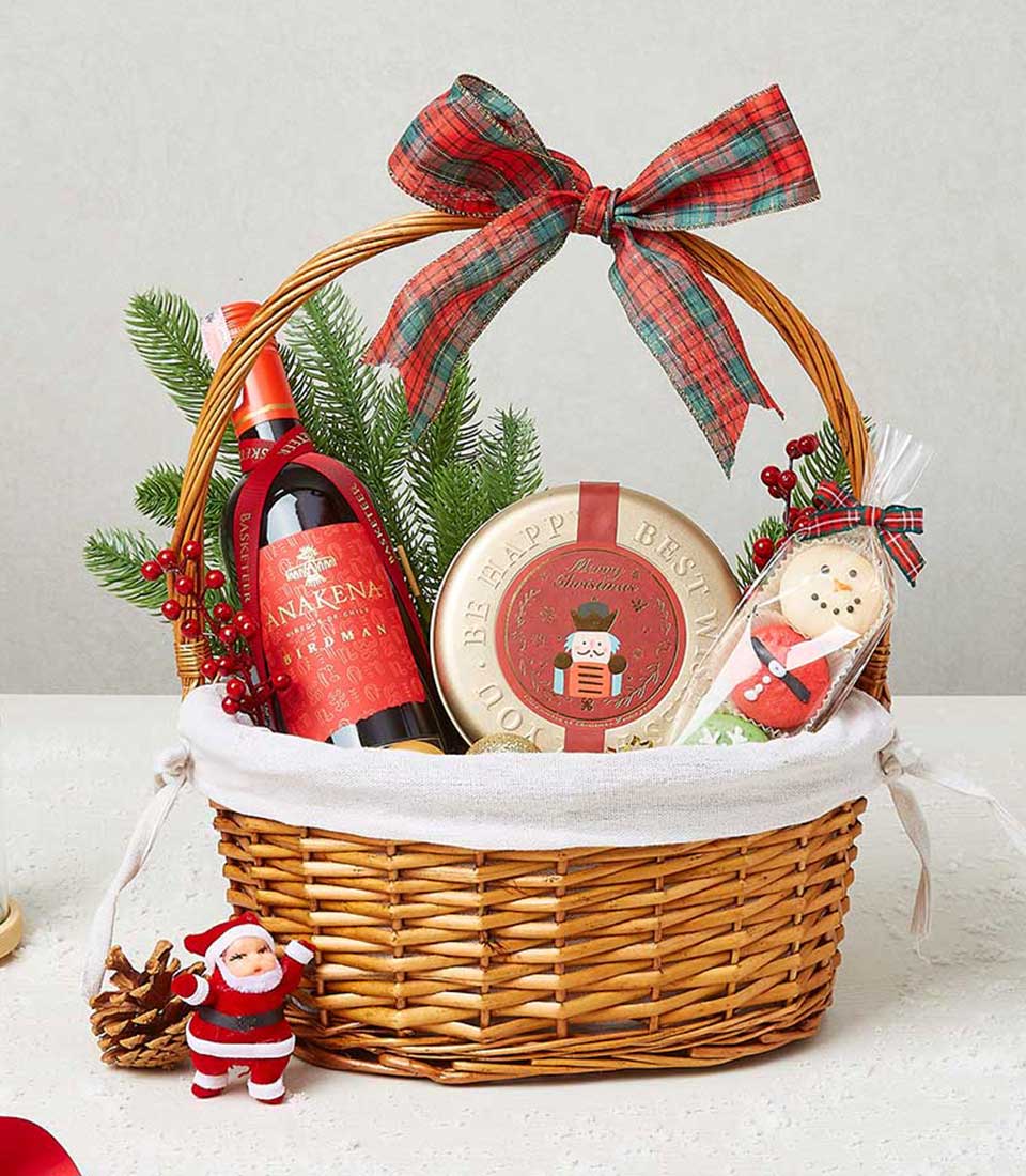 Festive wicker gift basket with red wine, nutcracker tin, and Christmas cookies tied with plaid ribbon