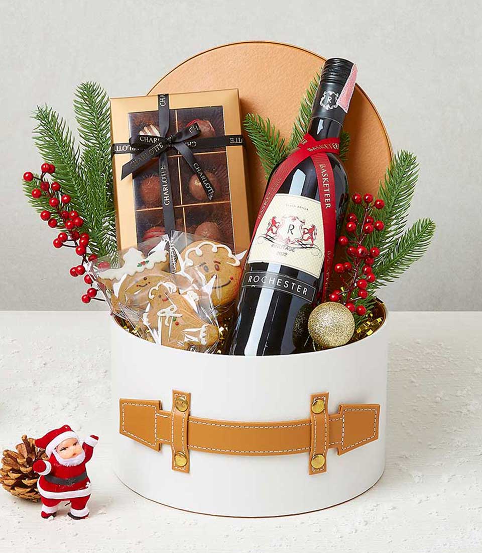 Festive wine gift box with red wine, chocolate, gingerbread cookies, pine and gold accents for Christmas