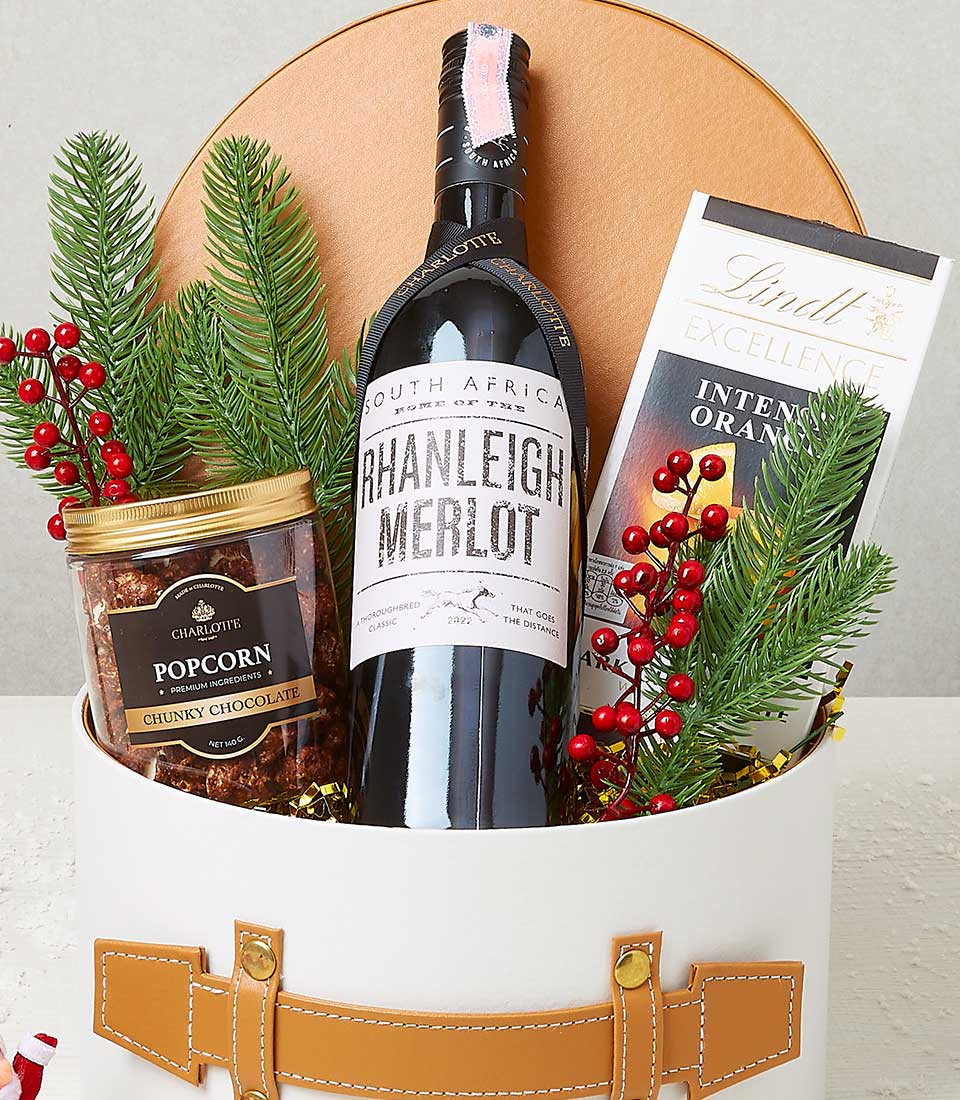 Premium red wine, artisan popcorn, and Lindt chocolate in leather-trimmed holiday gift box with festive greenery
