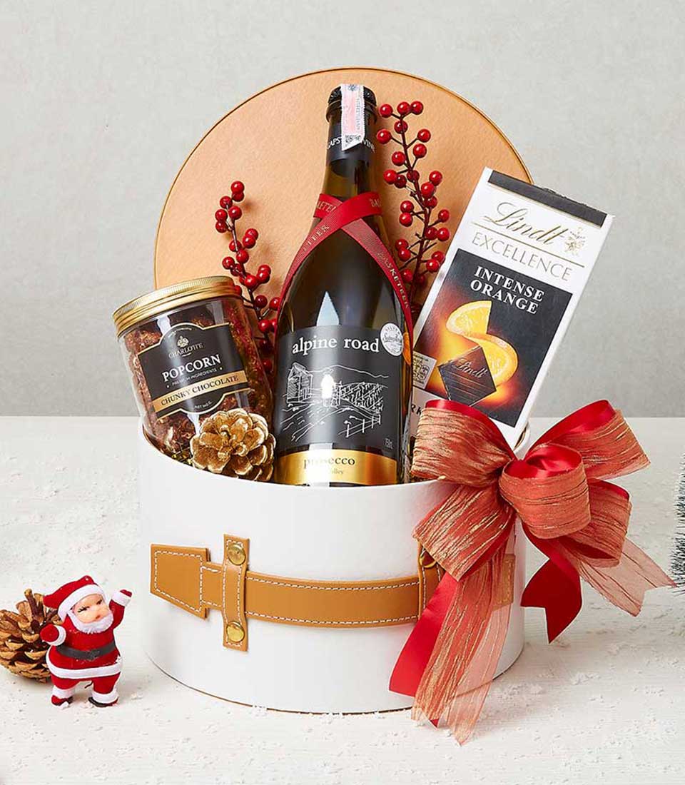 Yuletide Delights wine gift box with sparkling wine, gourmet popcorn, and chocolate in white cylindrical hamper with red and