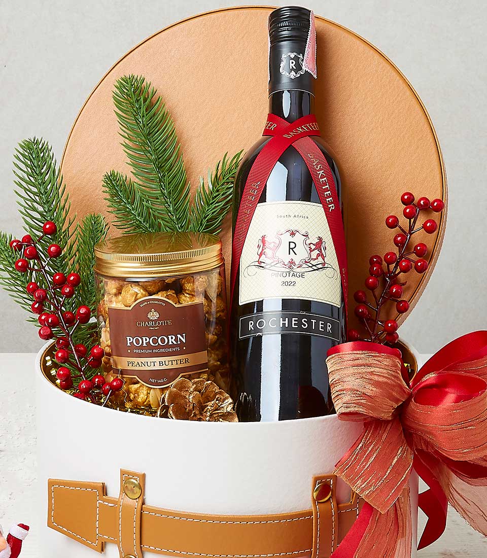 Premium red wine and gourmet popcorn in festive white gift box with gold accents and holiday greenery