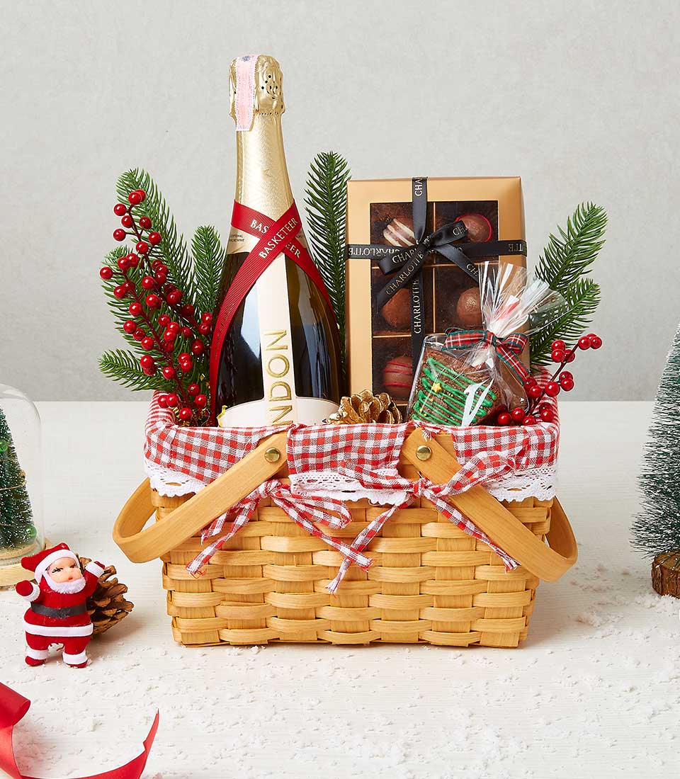 Festive sparkling wine, chocolates, and treats in red gingham-lined wicker basket with holiday decorations