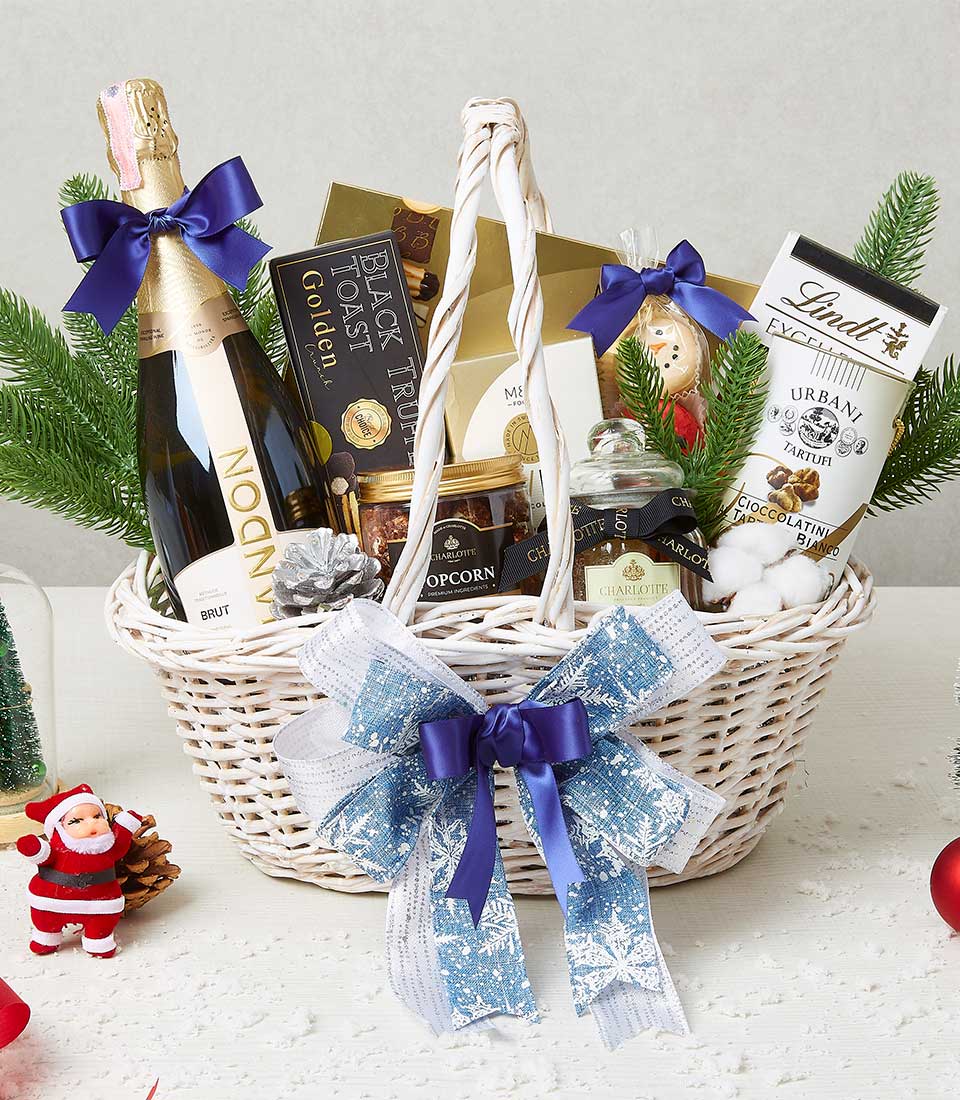 Festive white wicker Christmas hamper with sparkling wine, black truffle treats, gourmet jars, and holiday decorations