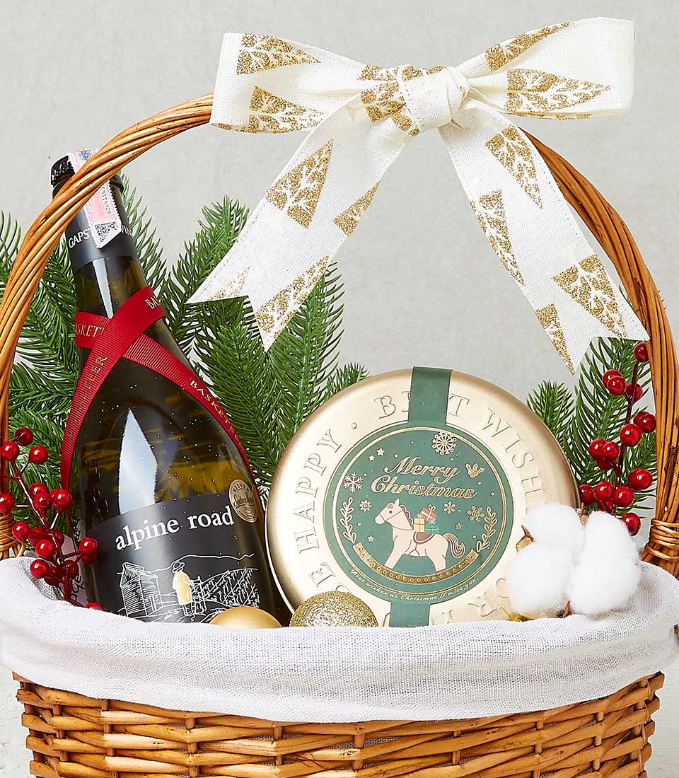 Festive Christmas wine gift basket with alpine road bottle, gold holiday tin, green pine, and white ribbon bow