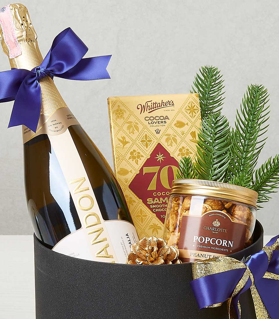 Luxury festive gift box with sparkling wine, Belgian chocolate, and gourmet popcorn in black cylindrical packaging, accented