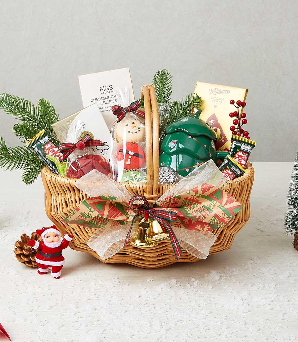 Woven wicker Christmas gift basket with holiday treats, KitKat, cheese crisps, cookies, chocolates, red berries, pine