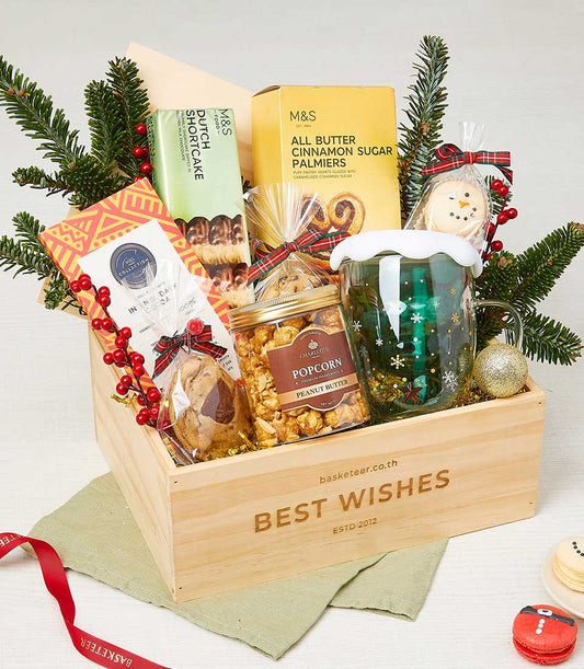 Wooden Christmas gift crate with festive treats, snowflake mug, and pine branches with red berries