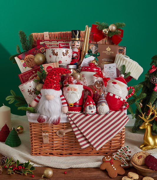 Festive Christmas gift basket with reindeer mug, gnome plush, Santa mug, cookies, and chocolate in wicker with red velvet bow
