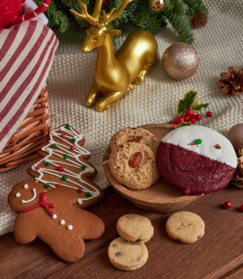 Premium Christmas cookie gift basket with gingerbread, festive decorations, and holiday treats on cream knit blanket