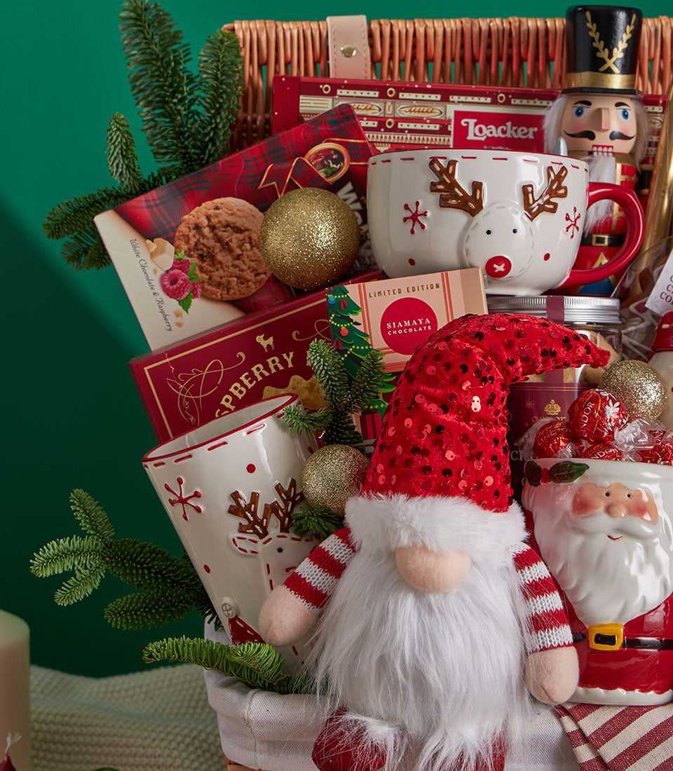 Premium Christmas gift basket with reindeer mugs, festive chocolates, gourmet treats, and holiday decorations in wicker