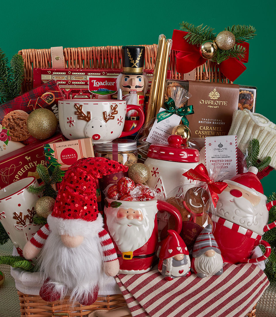 Festive Christmas gift basket with reindeer mug, Santa teapot, gingerbread cookies, nutcracker, and gold ornaments in wicker