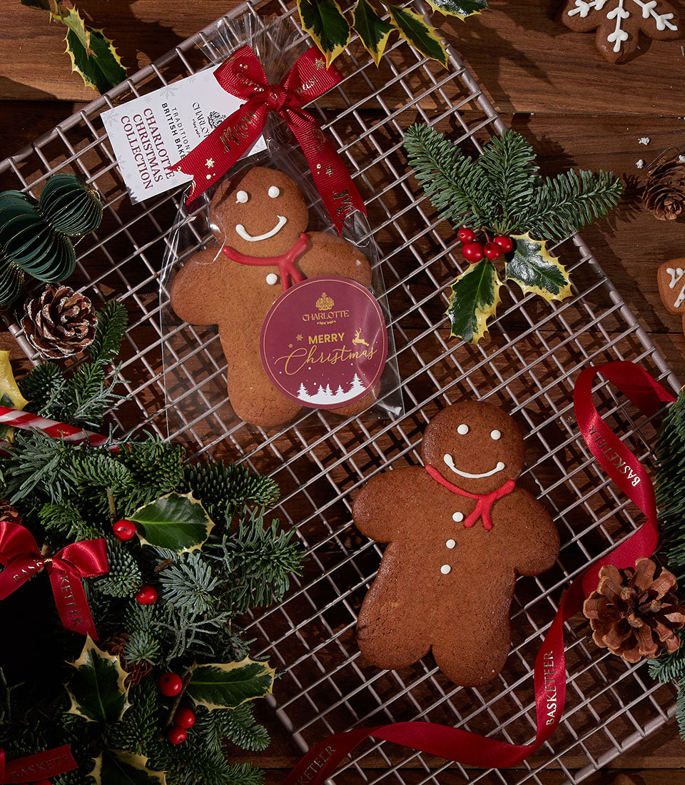 Gingerbread men cookies with white icing details and festive packaging, surrounded by pine branches and holly