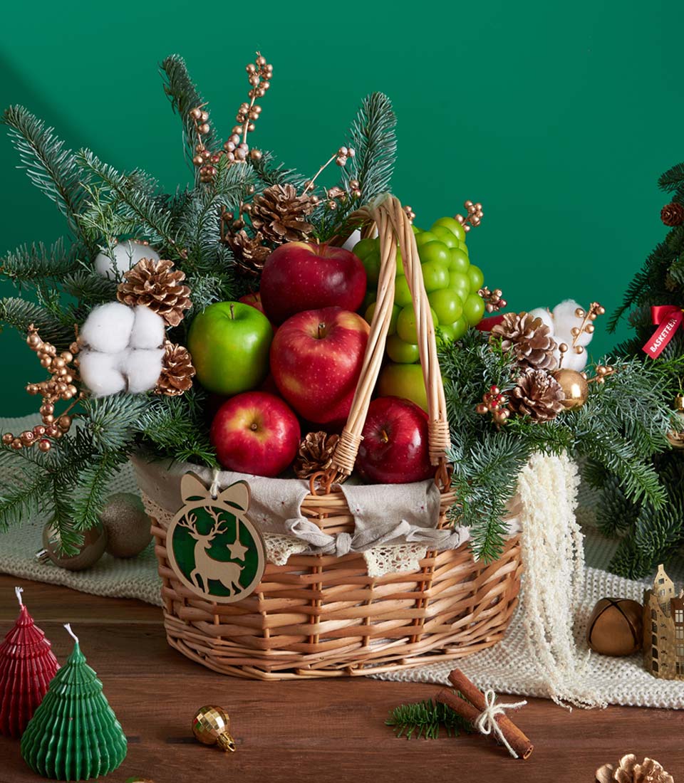 Classic green pine Christmas fruit basket with red and green apples, grapes, and festive holiday decorations
