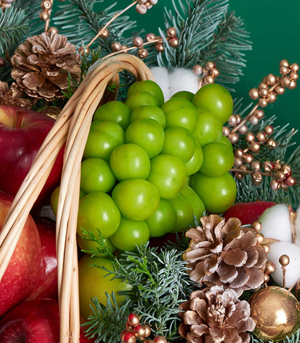 Festive wicker fruit basket with red apples, green grapes, and frosted pine branches for Christmas