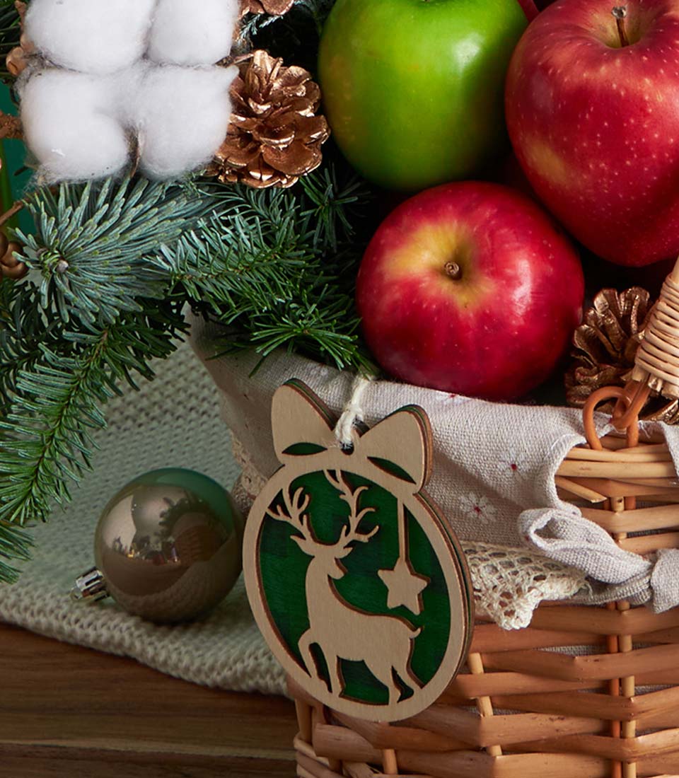 Festive Christmas fruit basket with red and green apples, pine, cotton, and wooden reindeer ornament