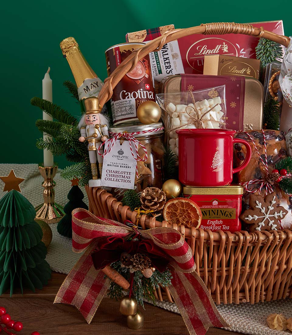 Woven wicker Christmas gift basket with red and gold ribbon, filled with sparkling wine, tea, chocolates, cookies,