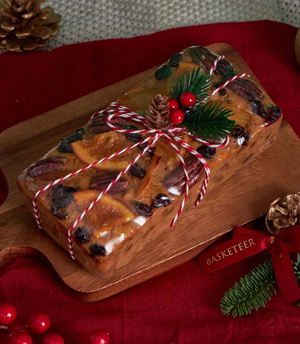 Luxury Christmas fruitcake gift basket with tea and chocolate on wooden board, decorated with pecans and candied citrus