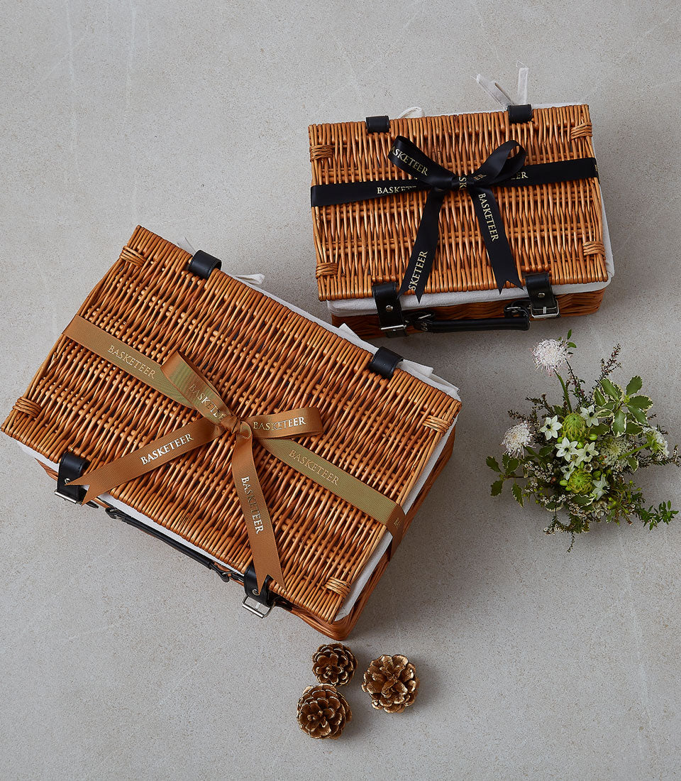 Wicker picnic hamper with leather straps, white ribbon, and coordinating floral accents for outdoor gatherings