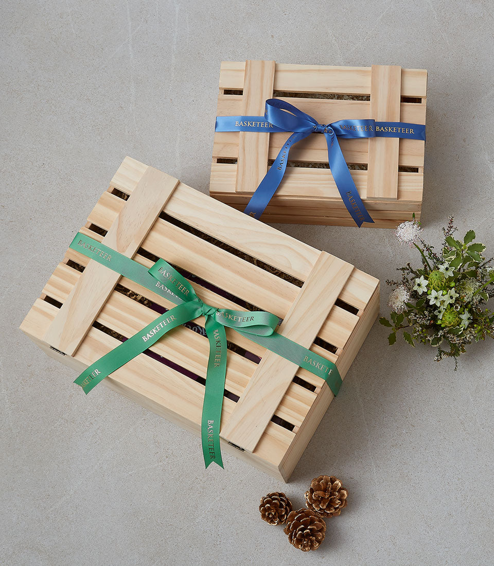 Basketeer premium hamper delivery Thailand, featuring gifts in wooden crates with blue and green Basketeer-branded ribbons. Corporate gift Bangkok option.
