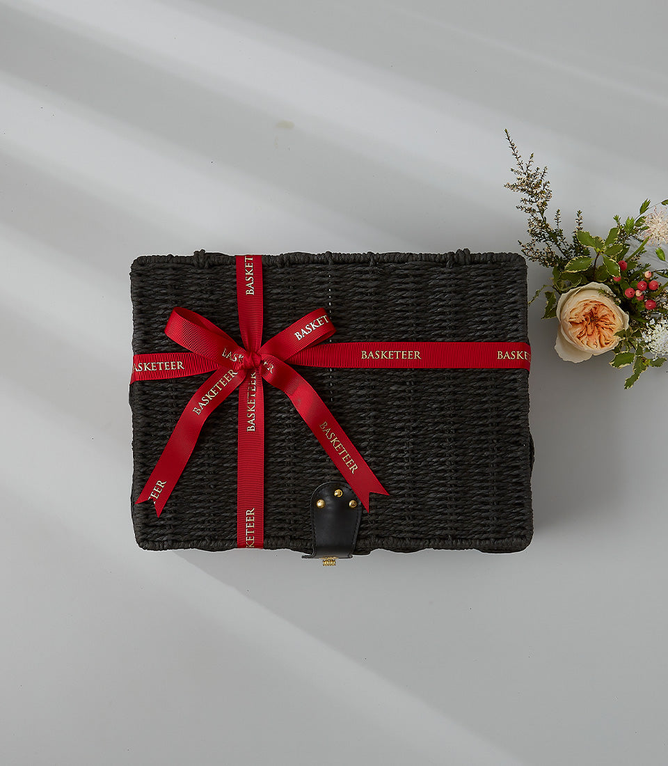 Black woven luxury gift basket with red satin Basketeer ribbon, paired with peach rose and white filler flowers
