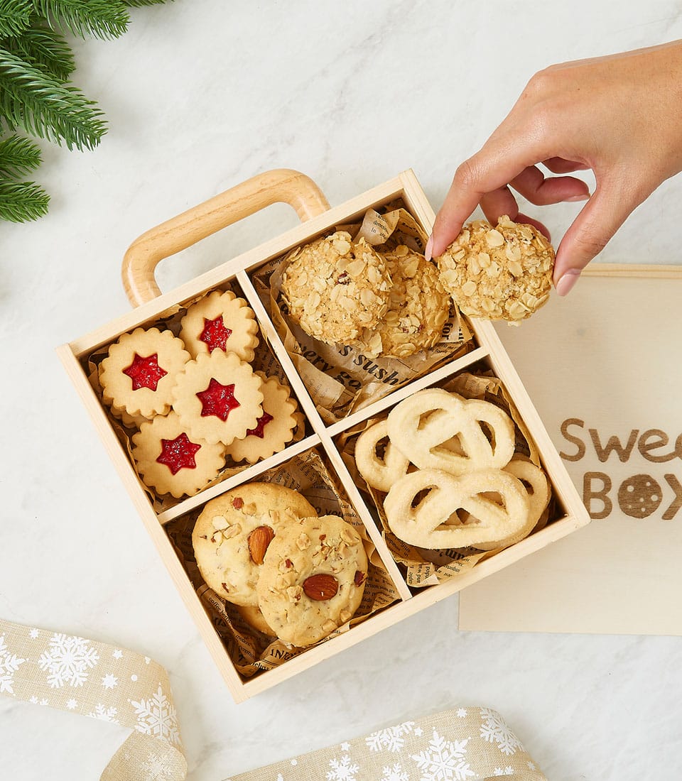 Wooden gift box with star shortbread, oatmeal, almond, and butter pretzel cookies on marble with festive ribbon