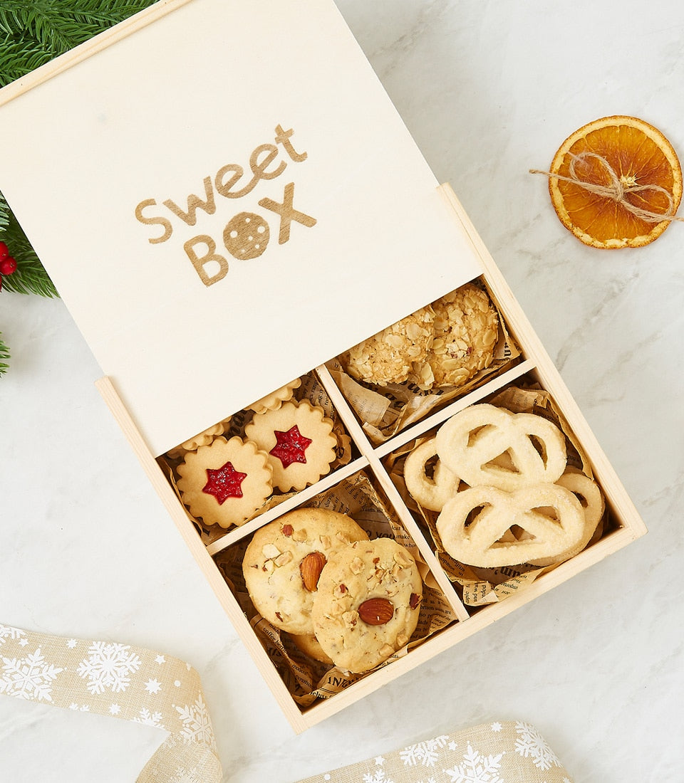 Wooden gift box with assorted gourmet cookies, jam-filled stars, almond rounds, and butter pretzels on marble with holiday