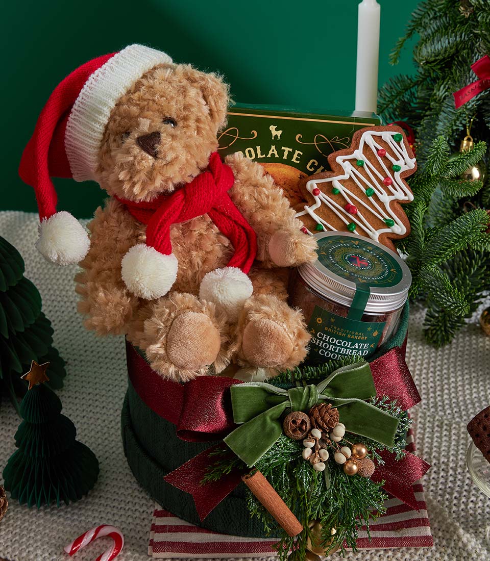 Festive Christmas gift box with teddy bear, chocolate, and gingerbread cookies in dark green packaging with red ribbon