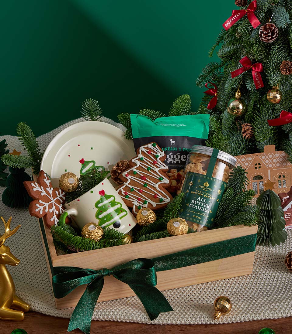 Festive wooden gift basket with gingerbread cookies, chocolates, ceramic mug and plate, green ribbon, holiday décor
