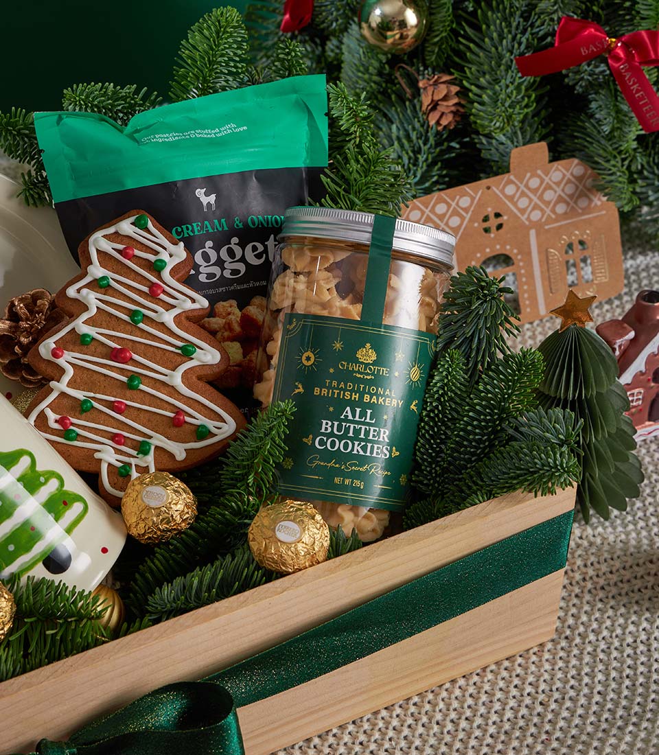 Festive Christmas gift basket with gingerbread tree cookie, butter cookies, chocolates, and pine branches in wooden crate
