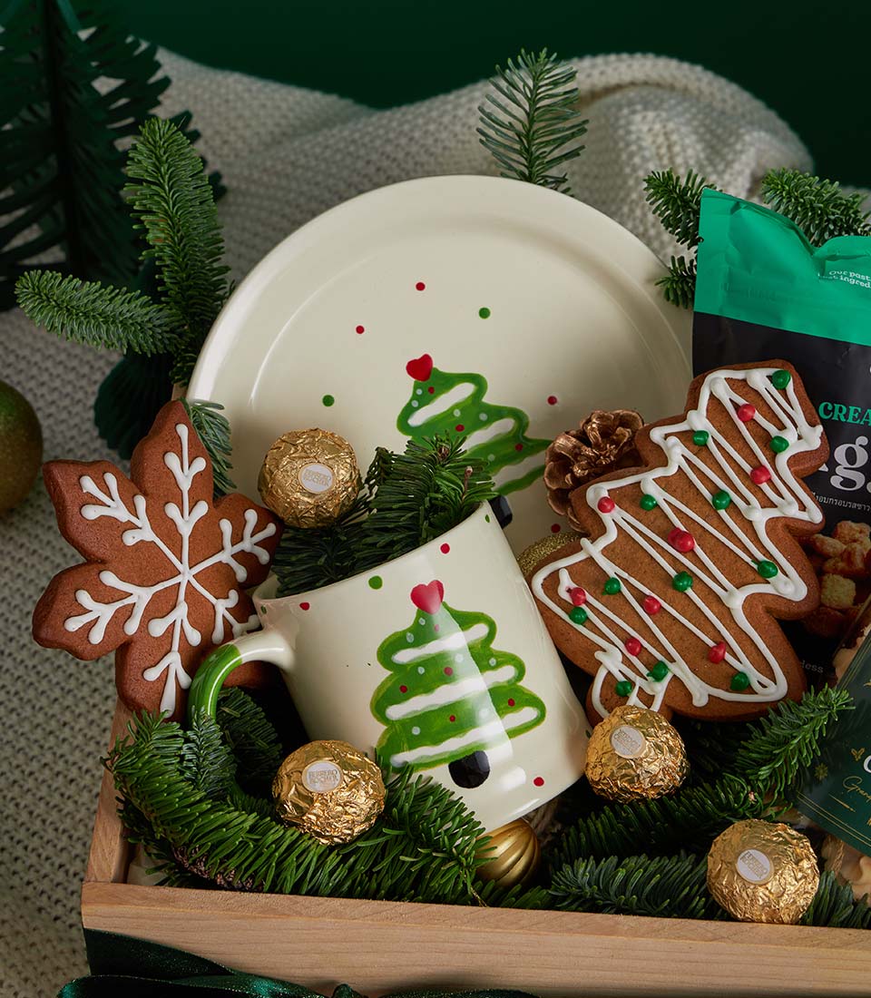 Festive Christmas gift set with ceramic plate and mug, gingerbread cookies, chocolates and snacks in wooden crate