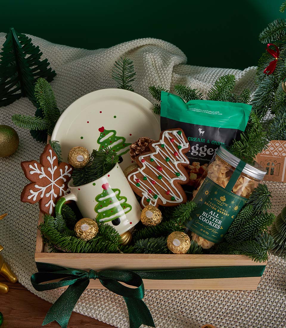 Wooden Christmas gift basket with festive ceramic mug, gingerbread cookies, butter cookies, and gold chocolates tied with